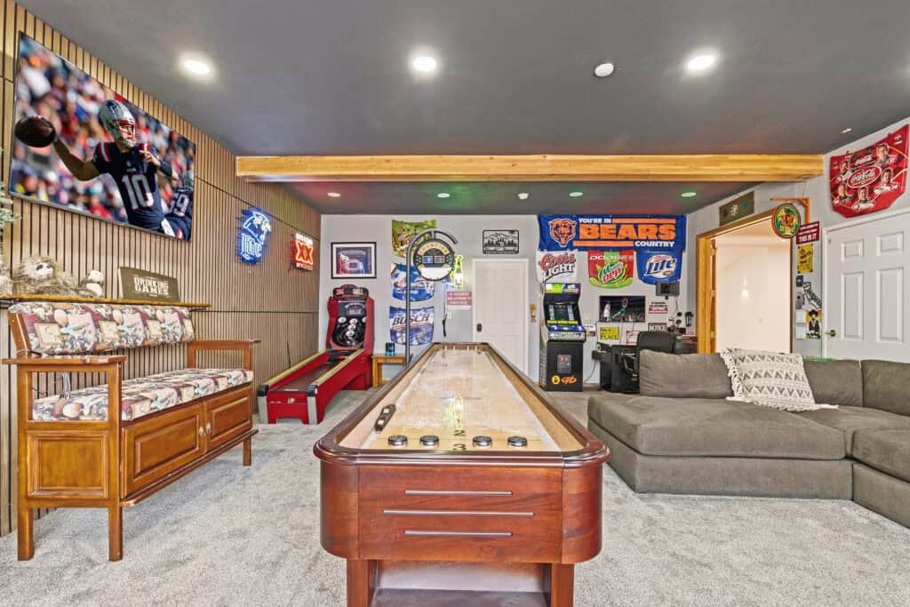 Indoor game room with arcade machines, sports memorabilia, and a shuffleboard table.
