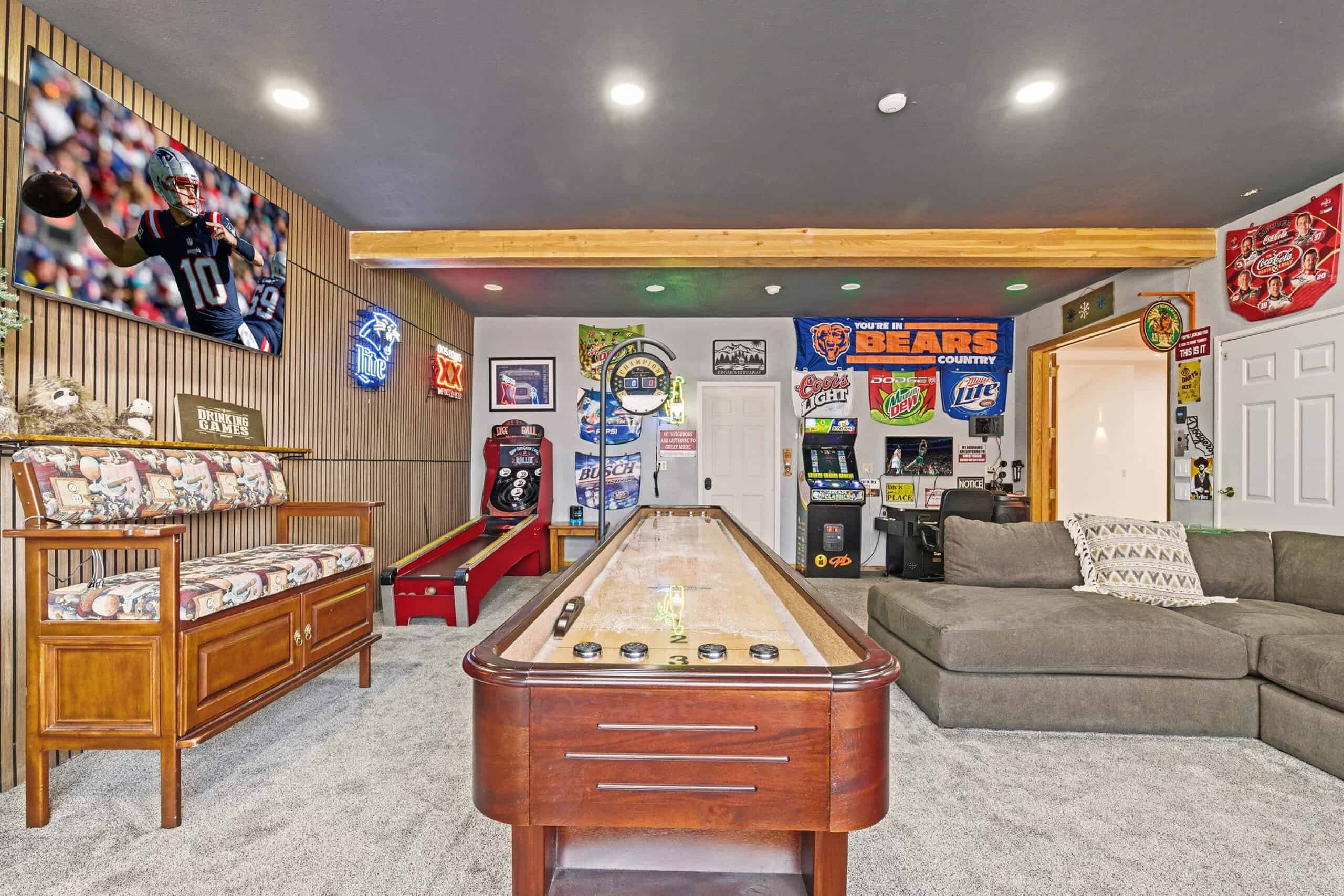 Indoor game room with arcade machines, sports memorabilia, and a shuffleboard table.