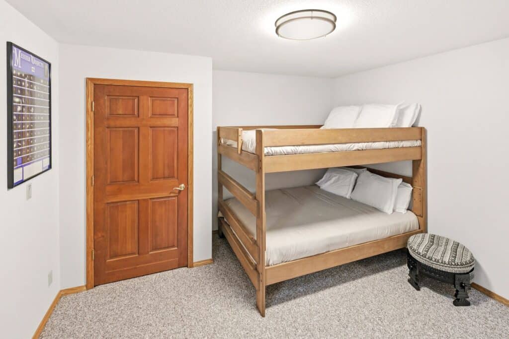 Wooden bunk bed in a small, clean bedroom with white walls and a closed wooden door.